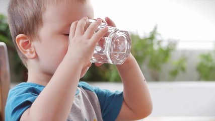 Cute baby boy drinking a glass of water in a cafe. Slow motion little boy drinking water. Close-up. The child is drinking a cup of water.