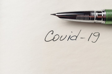 Covid-19 coronavirus inscription on a blank empty sheet of paper in a notebook. Nearby lies a pen....