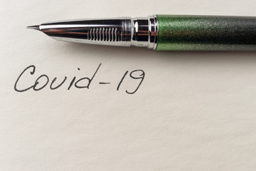 Covid-19 coronavirus inscription on a blank empty sheet of paper in a notebook. Nearby lies a pen....