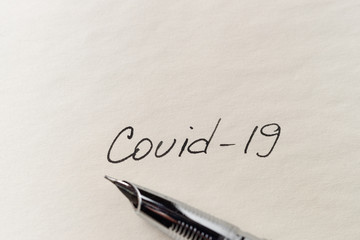 Covid-19 coronavirus inscription on a blank empty sheet of paper in a notebook. Nearby lies a pen....