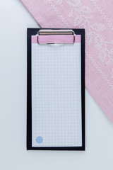 Notebook for notes on a white background. Nearby lies a pink napkin with embroidery.