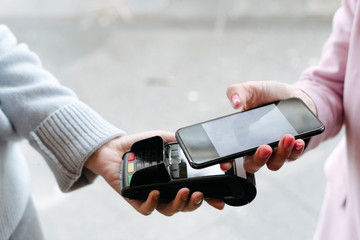 Hand of woman, paying cashless at POS terminal with her smartphone