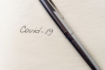 Covid-19 coronavirus inscription on a blank empty sheet of paper in a notebook. Nearby lies a pen....