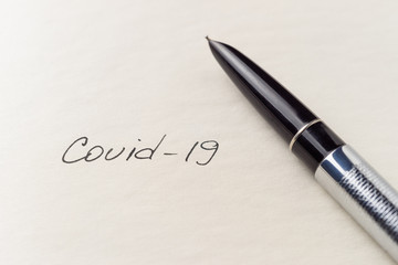 Covid-19 coronavirus inscription on a blank empty sheet of paper in a notebook. Nearby lies a pen....