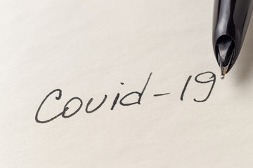 Covid-19 coronavirus inscription on a blank empty sheet of paper in a notebook. Nearby lies a pen....