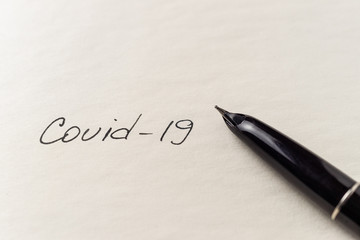 Covid-19 coronavirus inscription on a blank empty sheet of paper in a notebook. Nearby lies a pen. A lot of space for inscriptions and copyspace. Blank for inscriptions. Template for article or cover.