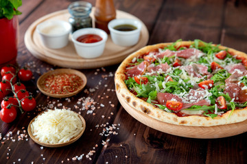 Italian pizza with arugula, cheese, ham. Top view. Pizza sauce, cherry tomatoes, salt, basil