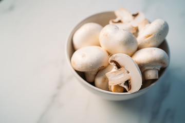 Set of fresh whole and sliced ​​champignons mushrooms in a bowl isolated on white stone background. Top view