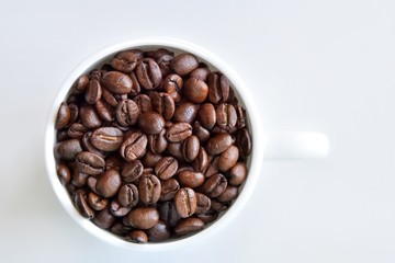 Roasted coffee beans in porcelain mug with selective focus on neutral background. Arabica coffee seeds in the coffee cup. Breakfast concept.