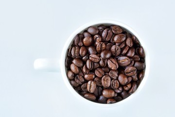 Roasted coffee beans in porcelain mug with selective focus on neutral background. Arabica coffee seeds in the coffee cup. Breakfast concept.