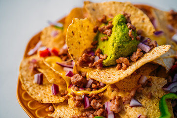 Close up of a plate of delicious Tortilla nachos corn chips with melted cheese sauce, ground beef, jalapeno peppers, red onion, salsa, and sour cream with guacamole dip. Top view