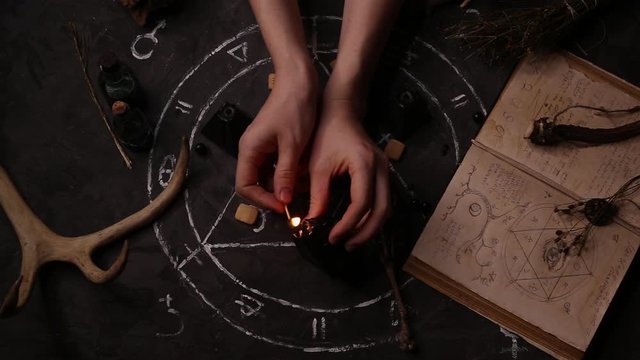 Top view of a female witch fortune teller girl lights magic black candles against the background of the pentagram.