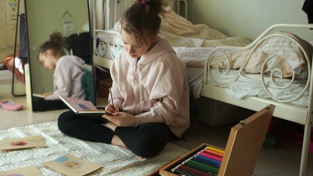 Schoolgirl draws drawings in a sketchbox with colored pencils. Shows his drawing and smiles. self-isolation and quarantine hobbies