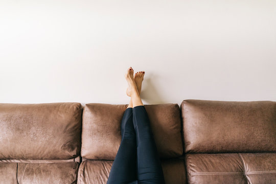 a woman's legs raised up high on the brown sofa at home