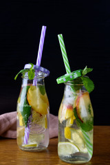 Refreshing fruit drinks with lemon, mint, peach in glass bottles and tubes on the table.