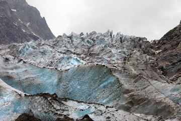 Glacier with deep crevasses covered with snow and ground in high rocky mountains