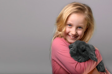 portrait of smiling little girl with rabbit posing in studio, kid girl is holding a little grey...