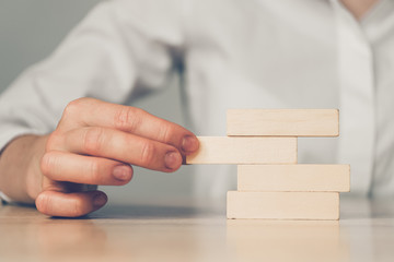 Cost reduction concept - abstractly a hand removes a wooden block from a pile.