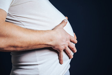 The guy has his hands on his fat stomach. Concept of disorder, bloating, overweight.