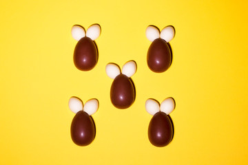 Rabbits made of chocolates and jelly in the center of a yellow background. Pattern for your easter design. There is space for text and there is nothing superfluous.