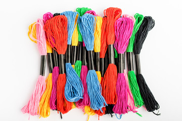 Fototapeta premium Many mixed vivid colored sewing threads for embroidery isolated on a white table, top view or flat lay of red, pink, yellow, blue, black and green textile materials 