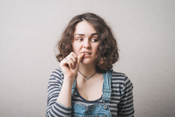 The woman lost in thought, chewing on nails from experiences fear. On a gray background.