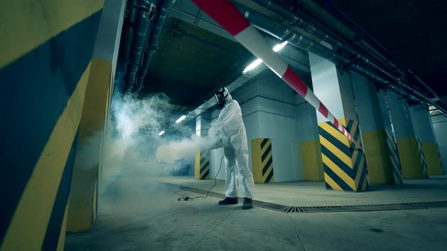 A person in a hazmat suit is decontaminating storage space. Worker disinfecting indoors using chemicals, coronavirus prevention concept.