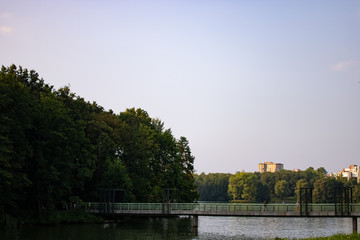 Obraz premium City park on a sunny summer day. Red wooden bridge over the river. City landscape