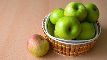 Wooden basket full of green apples on the table.