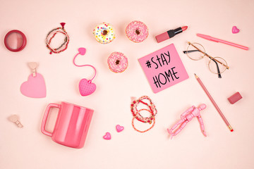 Flat lay with pink accessories, tea cup and donuts over light pink background. Top view. Morning rituals, stay at home idea