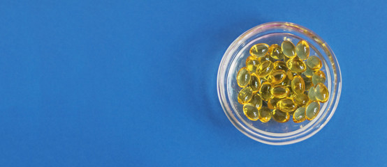 Yellow gelatin capsules with vitamin D3 in a glass container on a blue background. Pharmaceutical therapeutic and prophylactic preparation of vitamin D deficiency in adults and children.