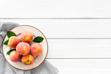 Summer lunch. Red peaches on white wooden background with tablecloth and leaves top-down copy space