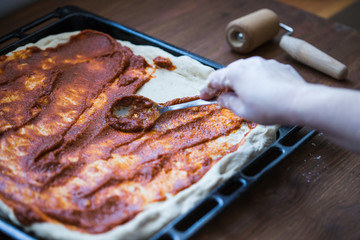 Photo of a person spreading tomato sauce on a pizza dough
