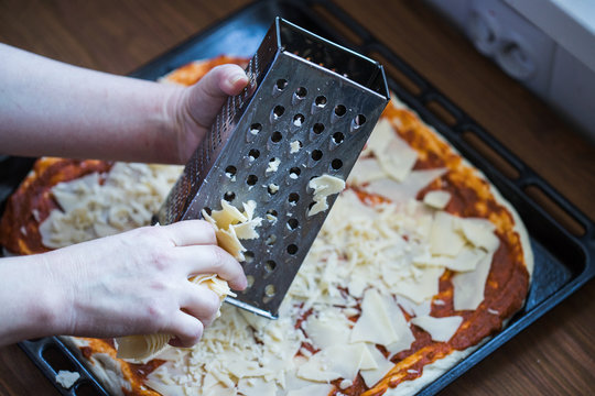 A photo of a person grating cheese on a pizza