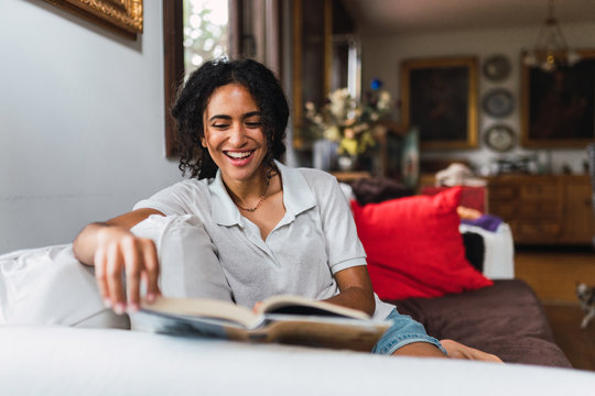 Pretty and happy curly hair girl with reading a book sitting on the sofa.