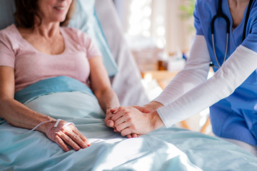 Unrecognizable doctor talking to senior patient in bed in hospital.