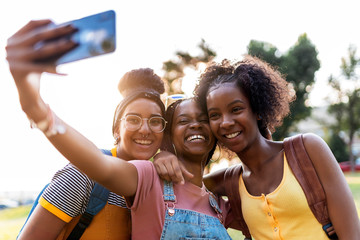Three smiling girl friends making selfie with smart phone.