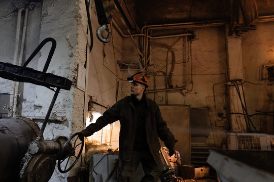 Factory employee pulling crucible and looking away