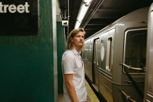 Man with long blonde curly hair waits for a train at a subway stop