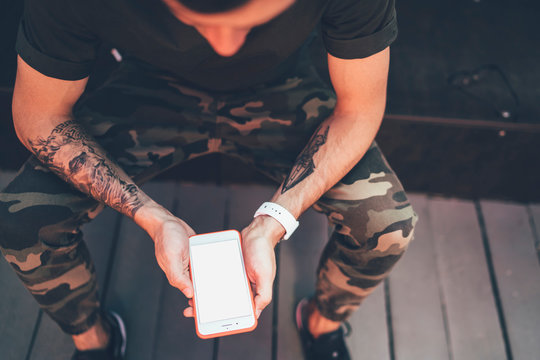 Cropped image of trendy hipster guy with tattooed hands installing application for playing online games on modern mobile gadget with copy space area for advertising text or website information