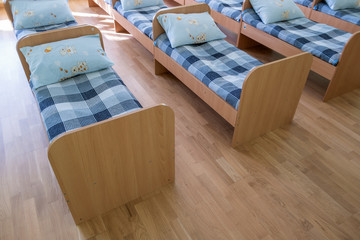 Many small beds with fresh linen in daycare preschool empty bedroom interior for comfortable...