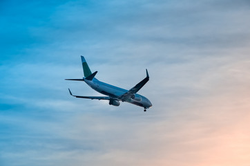 Large plane flies in the evening sunset sky, dramatic painted sky and airplane silhouette with clouds over Lisbon in Portugal.