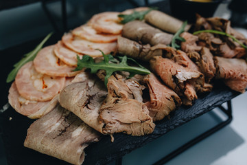 Thin slices of meat, ham, bacon lie on a white plate. The meat is planted on toothpicks, samples of products for testing.