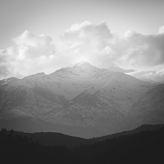 Conceptual black and white image of the brightened mountain peak , white clouds and dark forest in...