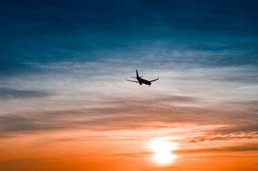 Large plane flies in the evening sunset sky, dramatic painted sky and airplane silhouette with clouds over Lisbon in Portugal.