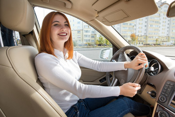 Fototapeta na wymiar Young redhead woman driver behind a wheel driving a car smiling happily.