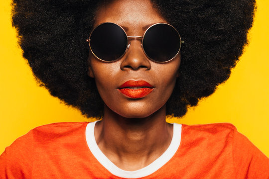 Beautiful Afro Woman posing over yellow background with round sunglasses
