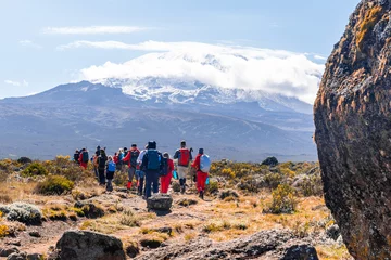 Foto op Plexiglas Kilimanjaro Groep trekkers die tussen sneeuw en rotsen van de Kilimanjaro-berg wandelen
