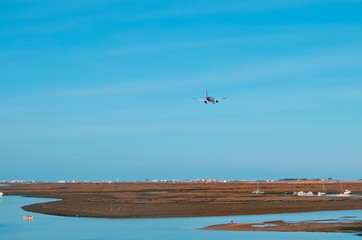 The plane flies to the airport over the river in the city of Faro in Portugal. Many boats on a...
