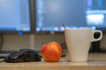White cup of coffee or tea, mouse controller and a red apple on blurred background of personal computer screen. © bilanol